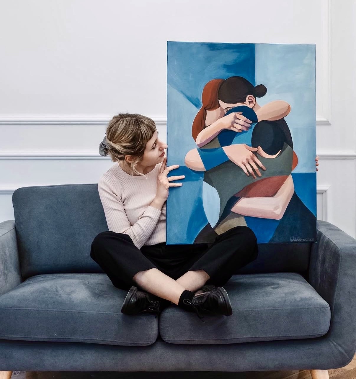 Artist sitting on a sofa holding a blue figurative painting